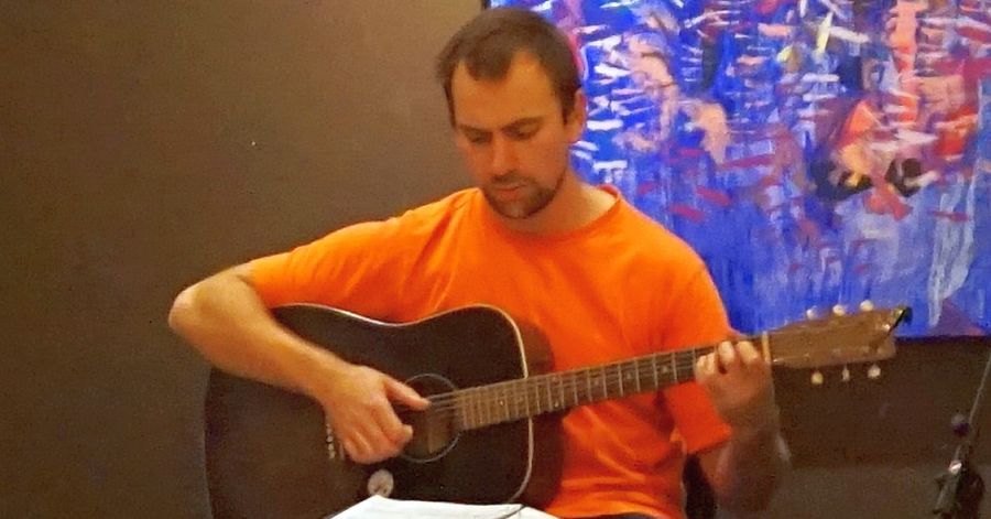 Brett in an Orange T-Shirt playing fingerstyle guitar at the Shaika Café