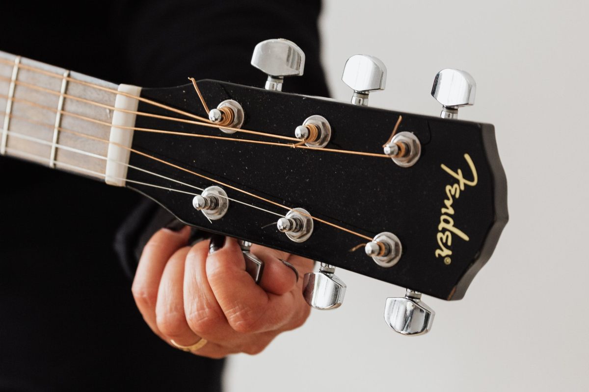 A hand tuning the first string on a black acoustic guitar.
