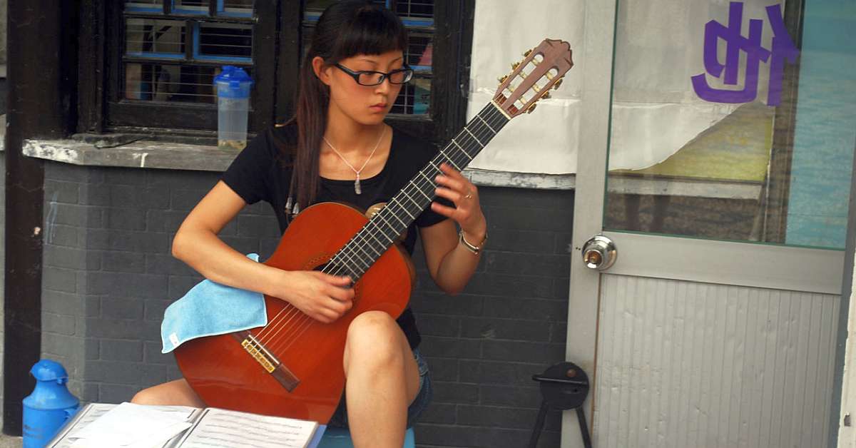 A Chinese woman dressed in black playing a classical guitar in the traditional position with the left leg raised.