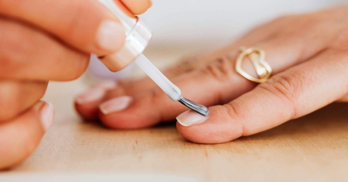 A close-up of a hand holding a brush applying acrylic mixture to the edge of the nail