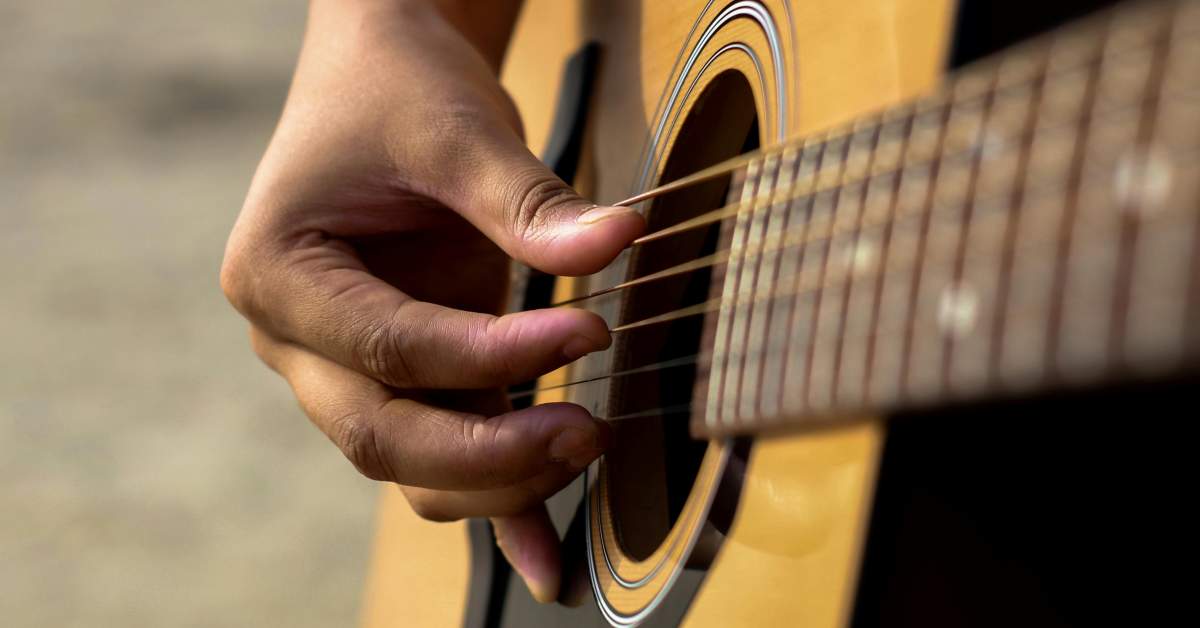 Closeup of the right hand of a fingerstyle guitarist using his pinky to steady the hand on the guitar
