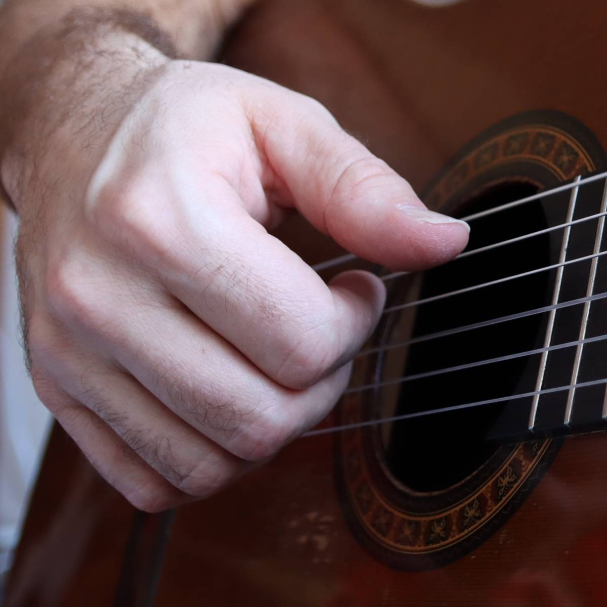 A right hand showing proper finger picking guitar technique on classical guitar for playing fingerstyle