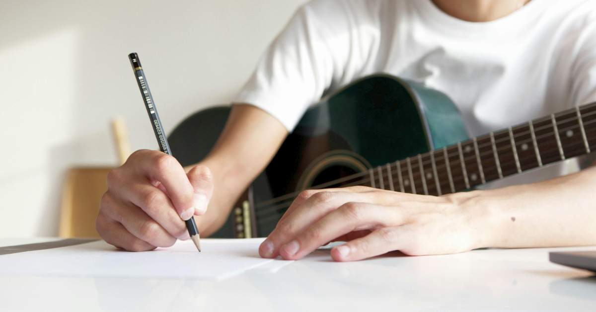 A guitarist writing musical notation on a sheet of paper