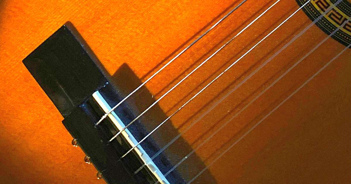 A close-up view of a set of ball-end strings on a classical guitar bridge