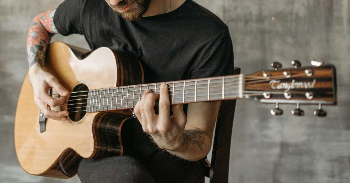 An acoustic guitarist with lots of tattoos playing a Tanglewood guitar