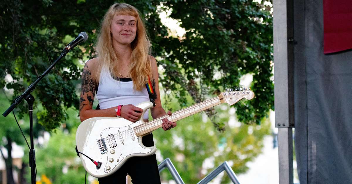 A girl in a white tank top smiling as she holds a white electric guitar
