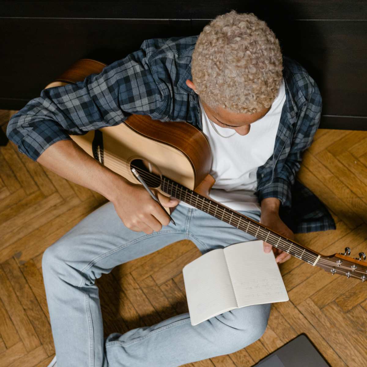 A man with an acoustic guitar writing in a journal and playing guitar