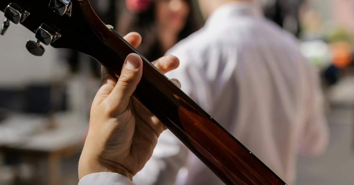 An image of the hand holding the neck of an acoustic guitar