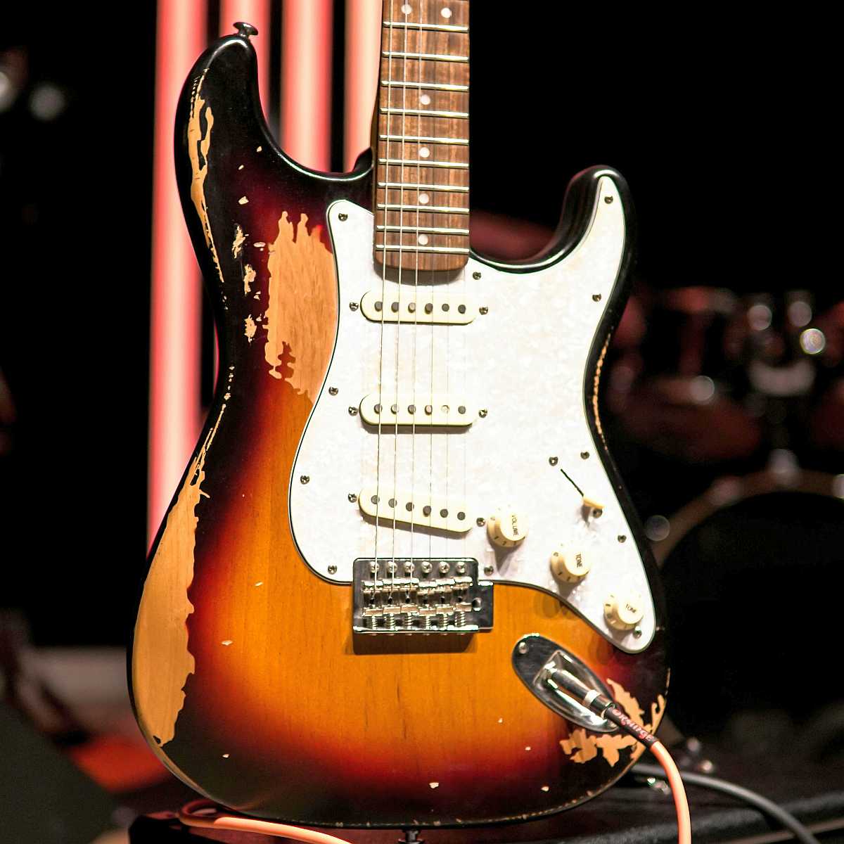 A fairly beat-up Fender Standard Stratocaster sitting plugged in on an amplifier